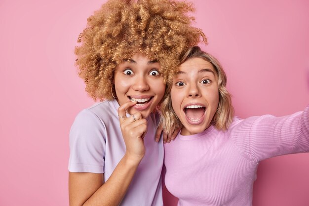 Una joven alegre se siente asombrada y llena de felicidad por hacer que la selfie se pare una al lado de la otra vestida casualmente aislada sobre un fondo rosa Autorretrato de amigas alegres