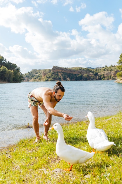 Foto gratuita joven, alimentación, gooses, en, orilla del río