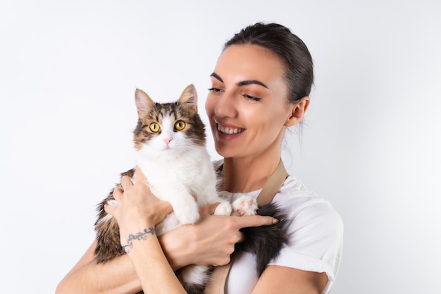 Una joven ama de casa con un delantal de fondo blanco sostiene a su querida mascota, un gran gato esponjoso, una familia feliz