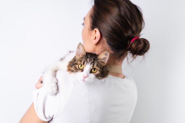 Una joven ama de casa con un delantal de fondo blanco sostiene a su querida mascota, un gran gato esponjoso, una familia feliz