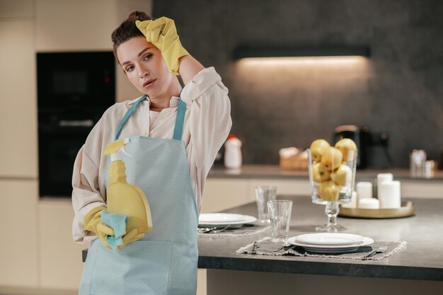 Joven ama de casa parada en la cocina y luciendo cansada después de limpiar