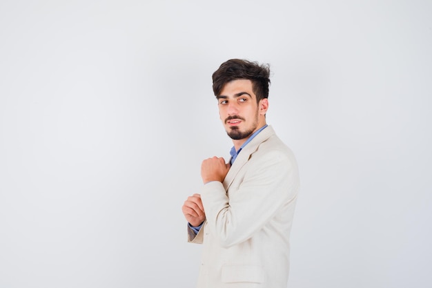 Joven apretando los puños en camisa azul y chaqueta de traje blanco y mirando feliz