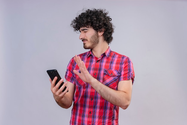 Un joven apuesto con cabello rizado en camisa a cuadros expresando negatividad sosteniendo teléfono