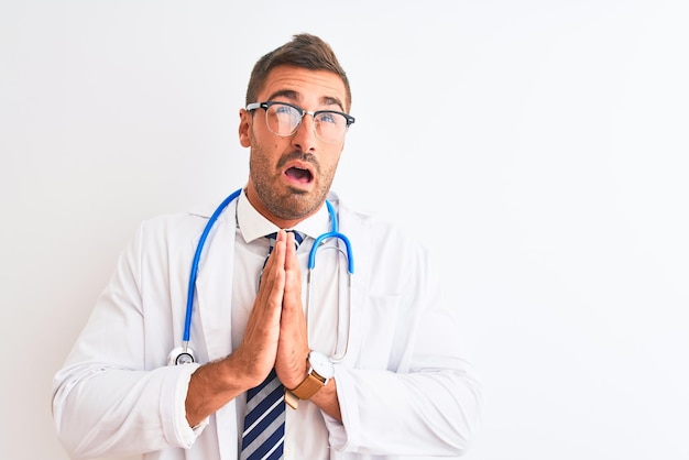 Foto gratuita joven apuesto doctor hombre con estetoscopio sobre fondo rogando y rezando con la mano