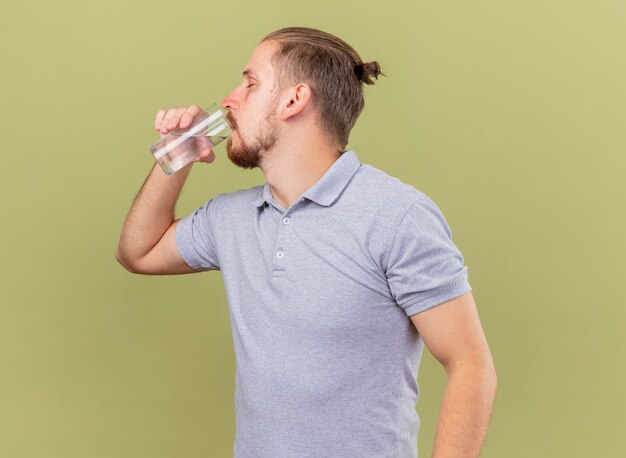 Joven apuesto enfermo eslavo bebiendo agua de vidrio con los ojos cerrados aislado sobre fondo verde oliva con espacio de copia