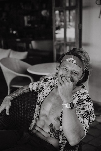 Joven apuesto hippie con un pañuelo rojo, con el torso desnudo en un café de bali. hombre feliz sonriendo