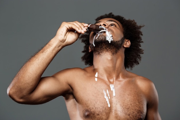 Joven apuesto hombre africano comiendo helado sobre fondo gris