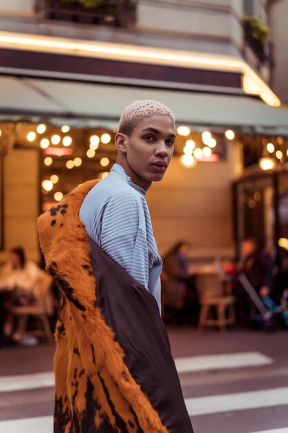 Joven apuesto hombre afroamericano posando al aire libre en París. sonrisa feliz, estilo de moda. luces de los cafés nocturnos.