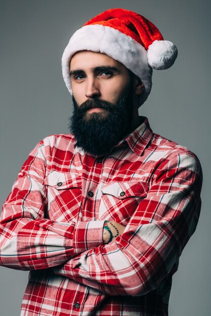 Joven apuesto hombre barbudo con sombrero rojo de navidad en pared gris