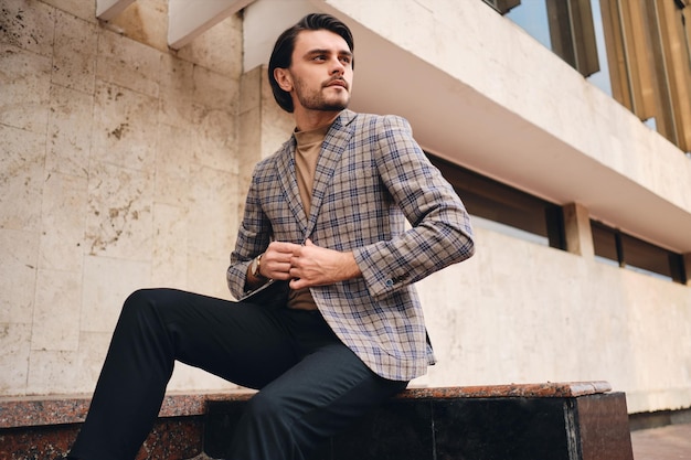 Foto gratuita joven apuesto hombre confiado en elegante chaqueta a cuadros mirando atentamente al aire libre