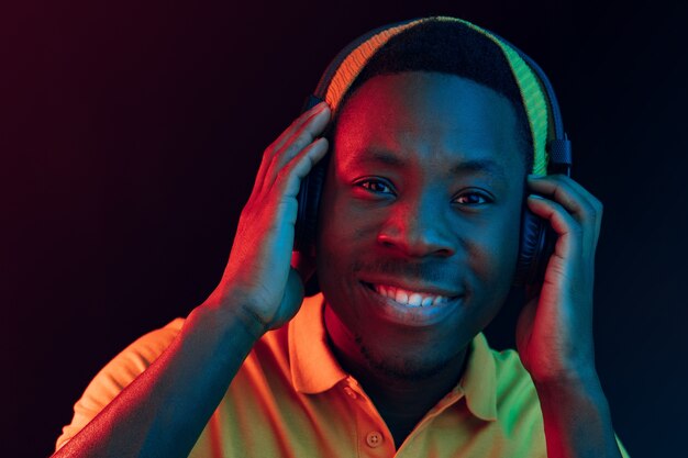 El joven apuesto hombre feliz hipster escuchando música con auriculares en el estudio negro