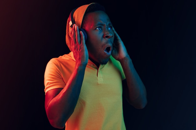 El joven apuesto hombre feliz hipster escuchando música con auriculares en el estudio negro