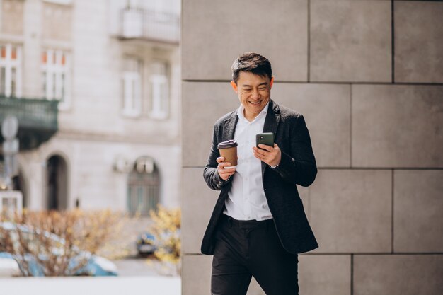 Joven apuesto hombre de negocios asiático en traje negro con teléfono y tomando café