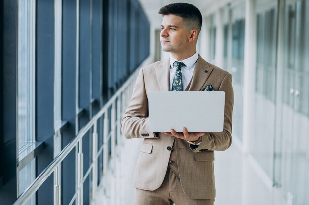 Joven apuesto hombre de negocios de pie con el portátil en la oficina