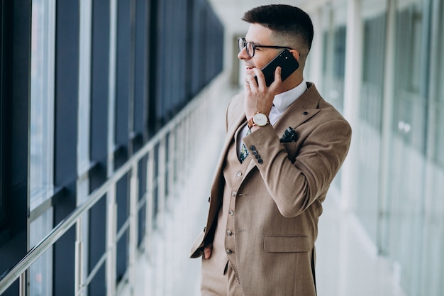 Joven apuesto hombre de negocios de pie con el teléfono en la oficina