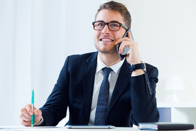 Foto gratuita joven apuesto hombre trabajando en su oficina con teléfono móvil.