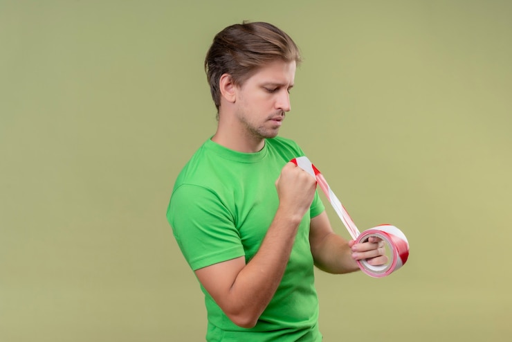 Foto gratuito joven apuesto hombre vestido con camiseta verde con cinta adhesiva en busca de confianza de pie sobre la pared verde 4