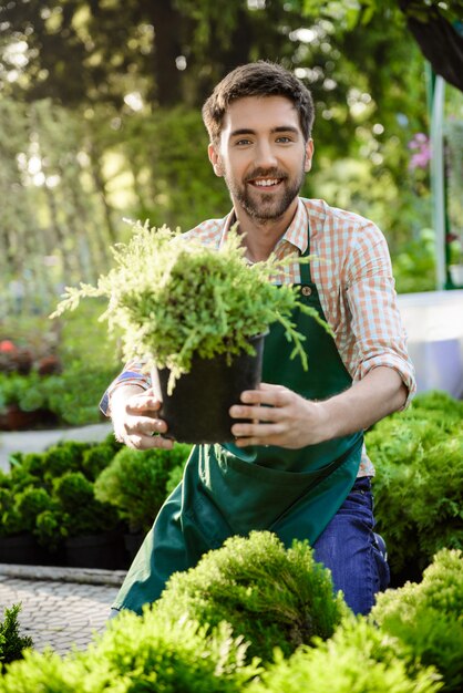 Joven apuesto jardinero alegre sonriendo, cuidando las flores