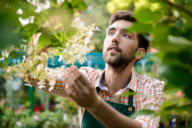 Joven apuesto jardinero alegre sonriendo, cuidando las flores