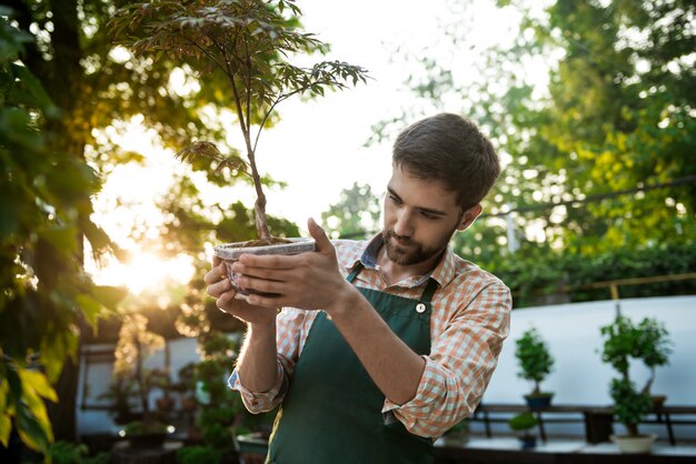 Joven apuesto jardinero alegre sonriendo, cuidando las plantas