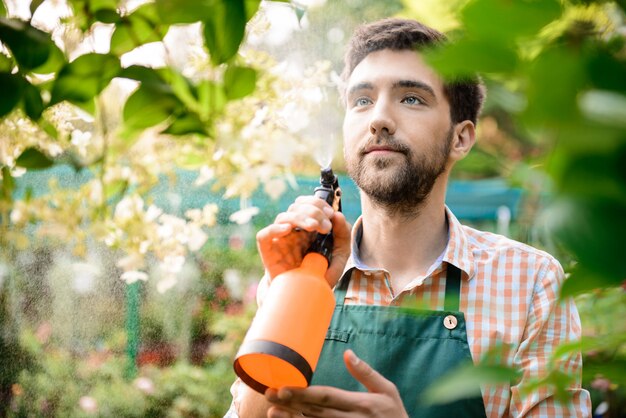 Joven apuesto jardinero alegre sonriendo, regando, cuidando las flores