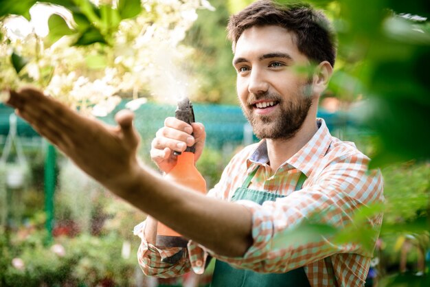 Joven apuesto jardinero alegre sonriendo, regando, cuidando las flores