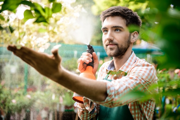 Joven apuesto jardinero alegre sonriendo, regando, cuidando las flores