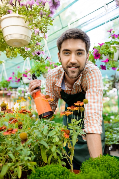 Joven apuesto jardinero alegre sonriendo, regando, cuidando las flores