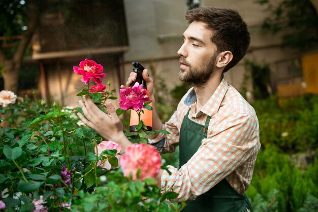 Joven apuesto jardinero alegre sonriendo, regando, cuidando las flores