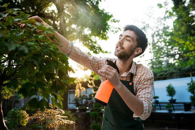 Joven apuesto jardinero alegre sonriendo, regando, cuidando las plantas