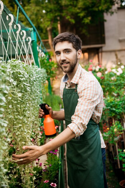 Joven apuesto jardinero alegre sonriendo, regando, cuidando las plantas