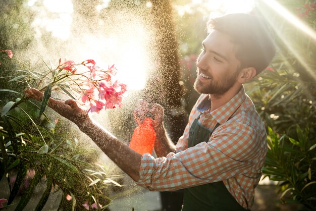 Joven apuesto jardinero sonriendo, regando, cuidando las flores