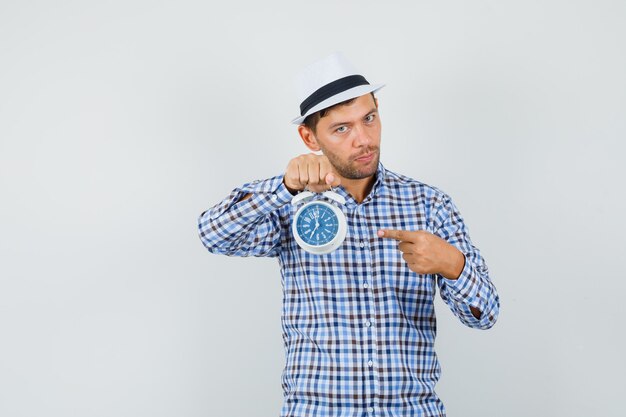 Joven apuntando al despertador en camisa a cuadros