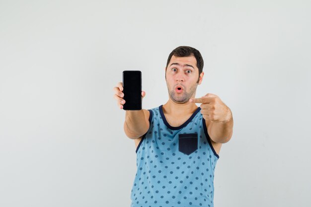 Joven apuntando al teléfono móvil en camiseta azul y mirando sorprendido