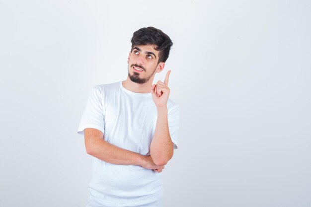 Joven apuntando hacia arriba en camiseta y mirando pensativo