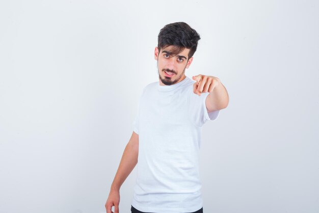 Joven apuntando a la cámara en camiseta y mirando confiado