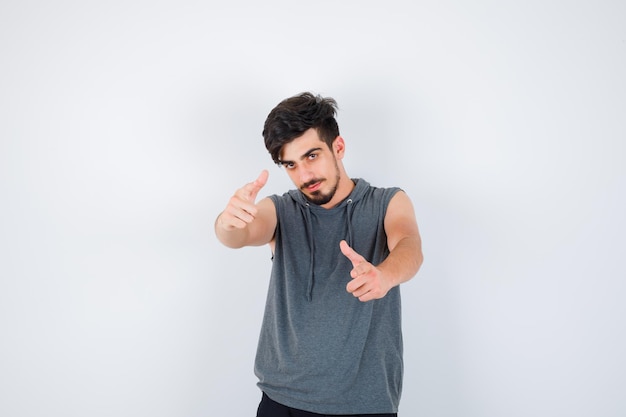 Joven apuntando a la cámara con los dedos índices en camisa gris y mirando serio