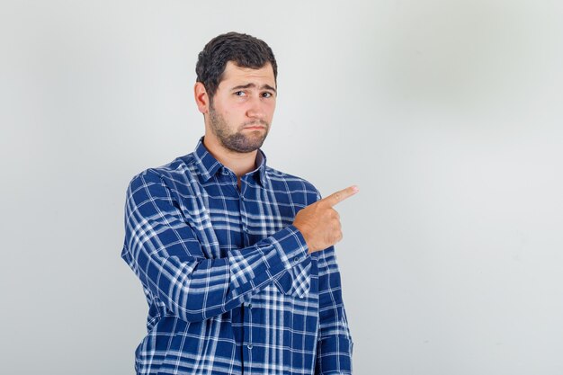 Joven apuntando con el dedo en camisa a cuadros y mirando molesto