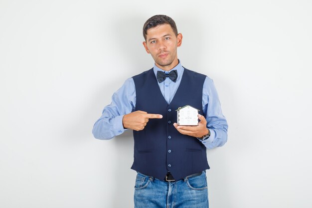 Joven apuntando con el dedo a la casa modelo en traje, jeans