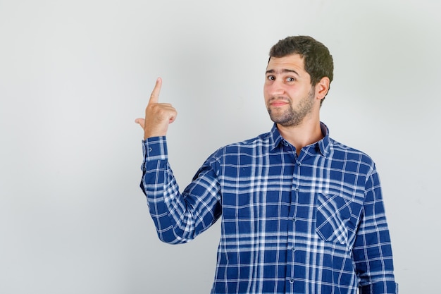 Foto gratuita joven apuntando hacia la espalda y sonriendo con camisa a cuadros