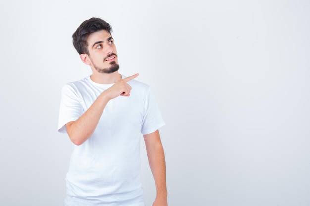 Joven apuntando a la esquina superior derecha en camiseta y mirando pensativo