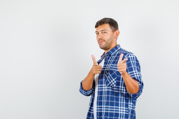 Joven apuntando con gesto de pistola en camisa y mirando confiado. vista frontal.