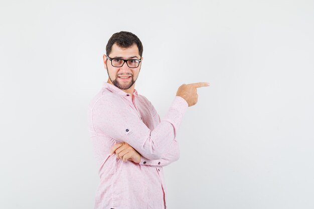 Joven apuntando hacia el lado en camisa rosa y mirando alegre