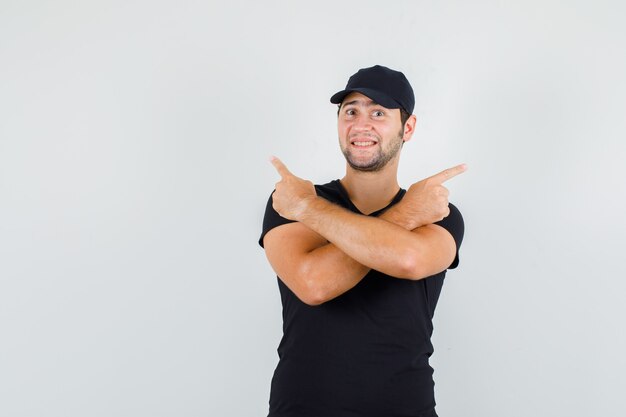 Joven apuntando a un lado en camiseta negra, gorra y mirando alegre.