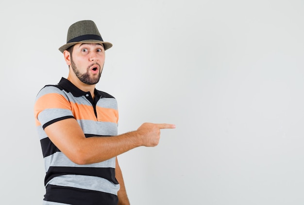 Joven apuntando hacia el lado en camiseta, sombrero y mirando se preguntó