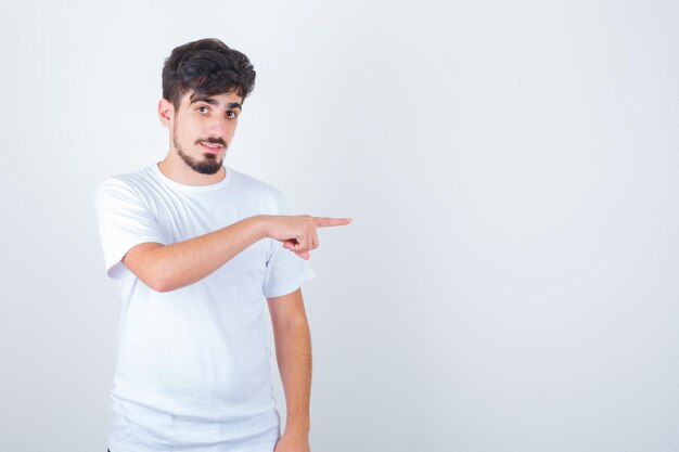 Joven apuntando hacia el lado derecho en camiseta y mirando confiado