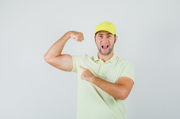 Joven apuntando a los músculos del brazo en uniforme amarillo y mirando poderoso