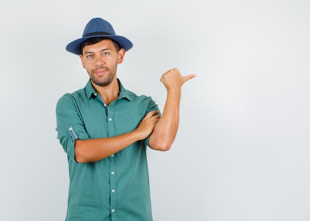 Joven apuntando con el pulgar a un lado y sonriendo en camisa