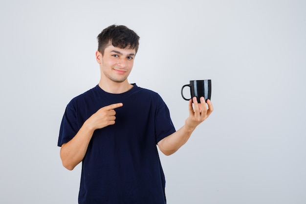 Joven apuntando a la taza en camiseta negra y mirando confiado, vista frontal.