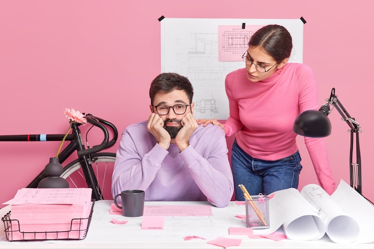 Foto gratuito joven arquitecta e ingeniero colaboran en un proyecto común. hombre barbudo aburrido triste posa en la oficina creativa con un colega cansado de trabajar en planos. concepto de trabajo en equipo